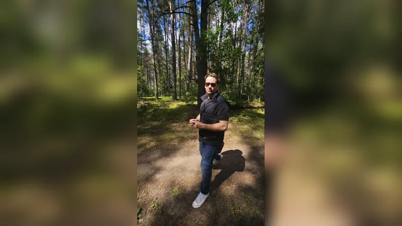Maksim standing on a forest path among pine trees